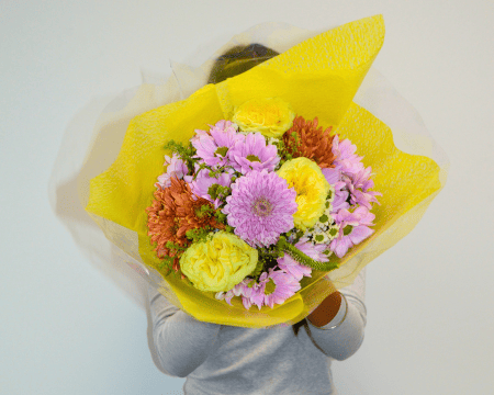 Person sitting cross-legged holding large yellow-wrapped bouquet of pink and yellow flowers
