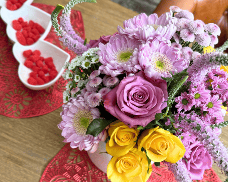 Valentine's Day table setting with pink and yellow flower arrangement on red lace heart placemat, heart-shaped bowls with red candy