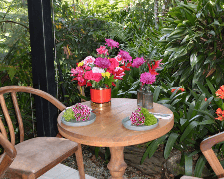 Lush red and pink flower arrangement in gold-trimmed red vase with garden backdrop