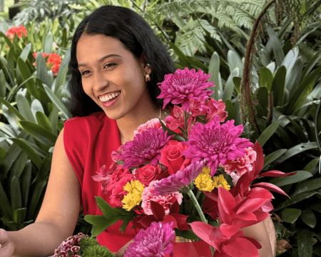Woman in red dress with vibrant flower arrangement in tropical garden setting